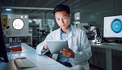 A young physician inside a research lab, reviewing information on a tablet